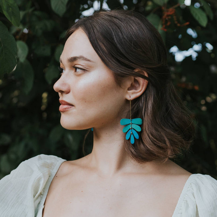 Woman wearing green leaf-shaped earrings against a natural background