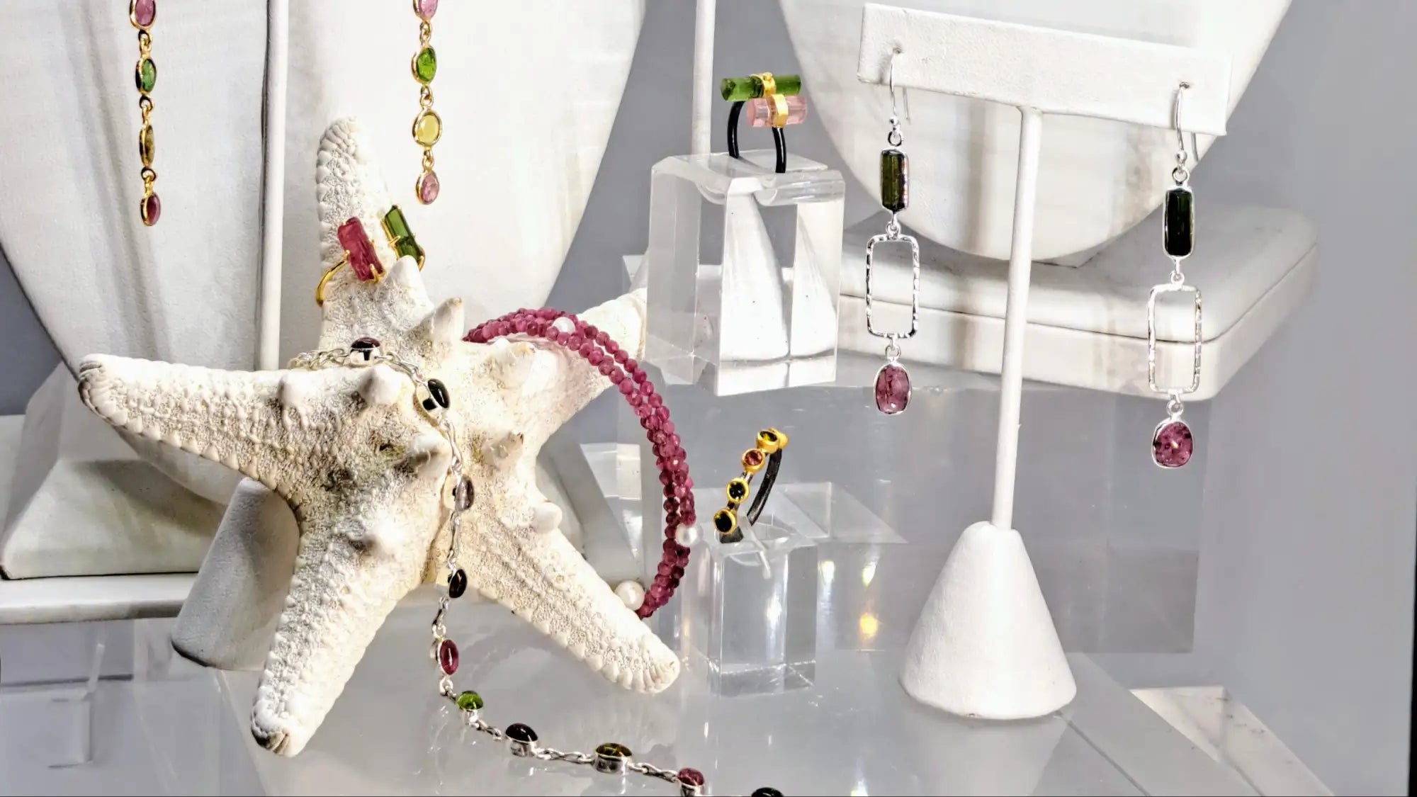 A delicate pink beaded bracelet with black and silver accents, elegantly draped over a white starfish.